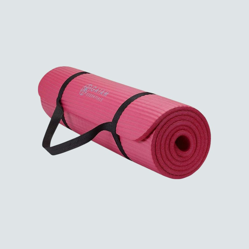Pink yoga mat with a black carrying strap on a light gray background