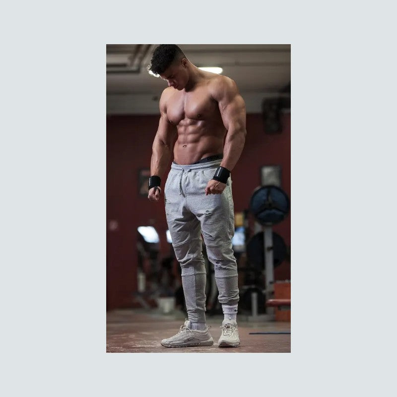 Muscular man in a gym wearing gray jogger pants and white sneakers.