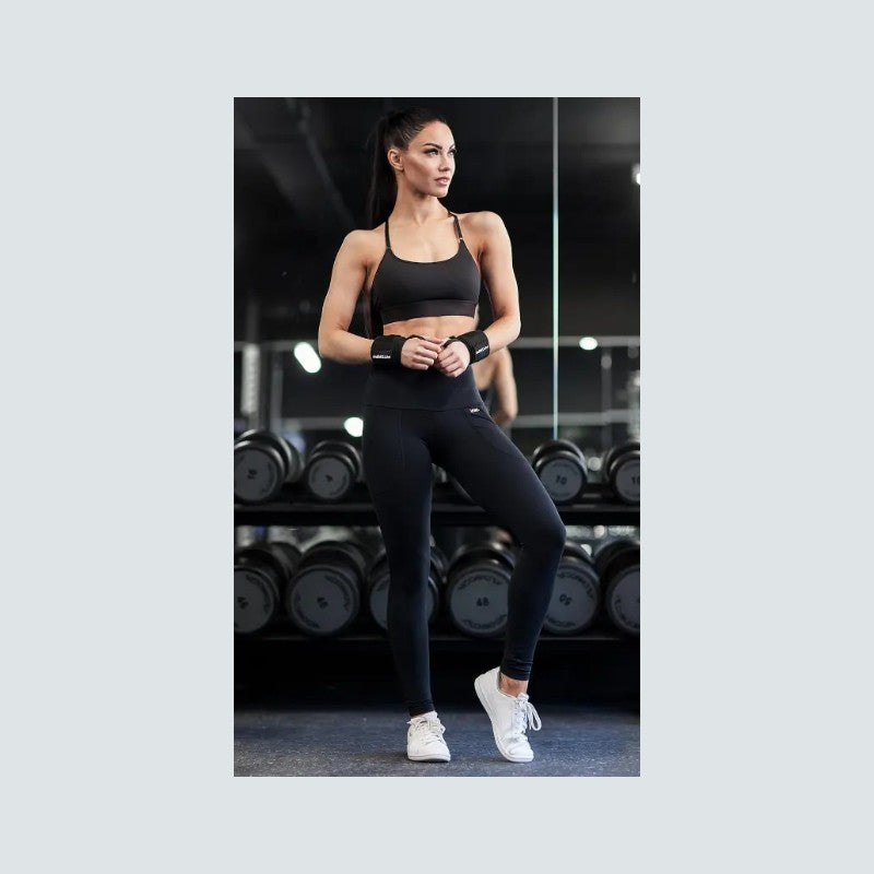 Woman in black athletic wear standing in a gym with weights in the background