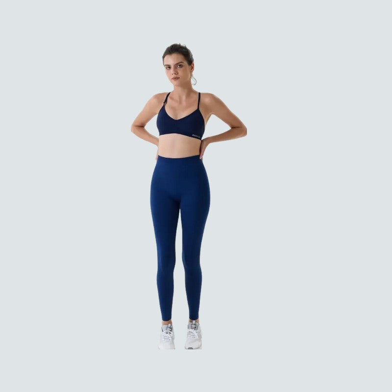 Woman wearing a navy blue sports bra and leggings set on a light gray background