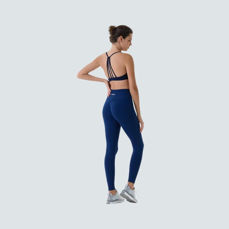 Woman wearing a navy blue sports bra and leggings on a light gray background
