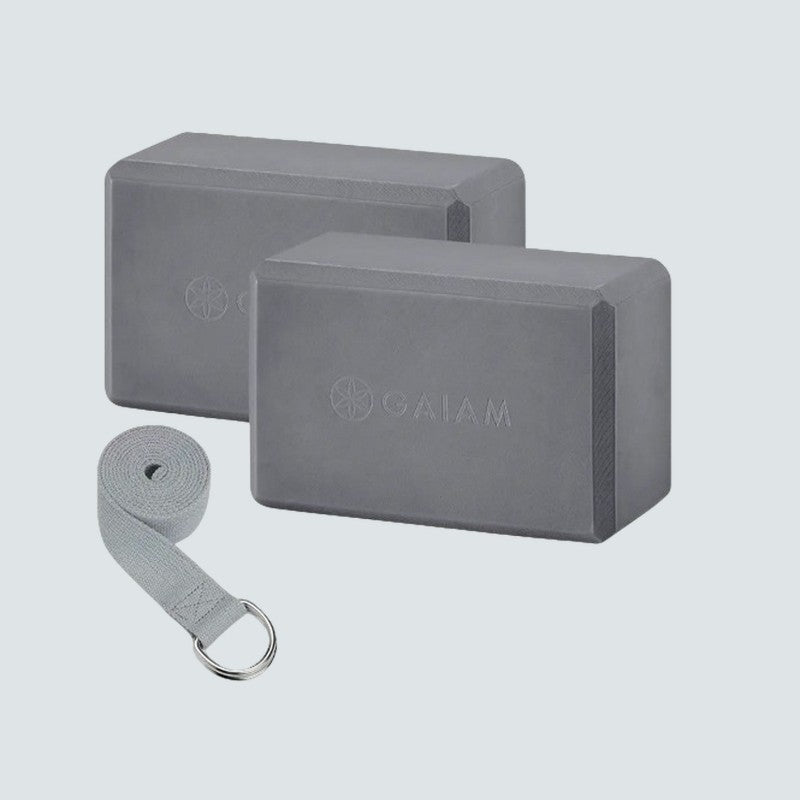Two gray yoga blocks with a strap on a light gray background, featuring the Gaiam brand.